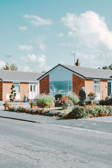 The image depicts a front garden area of a residential property with a neat and well-maintained landscape. The garden features a variety of colorful flowering plants and lush green foliage arranged in